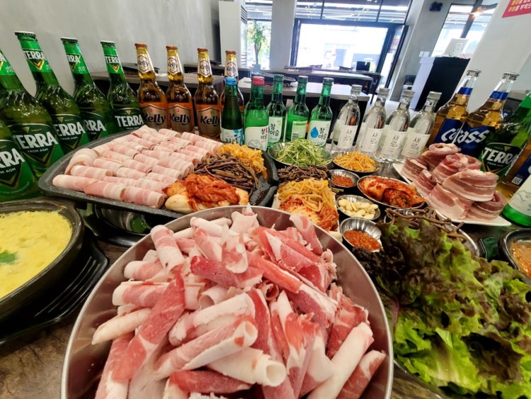 대패삼겹살과 차돌박이, 김치와 나물, 채소와 주류가 차려진 대패공장 실제 한 상